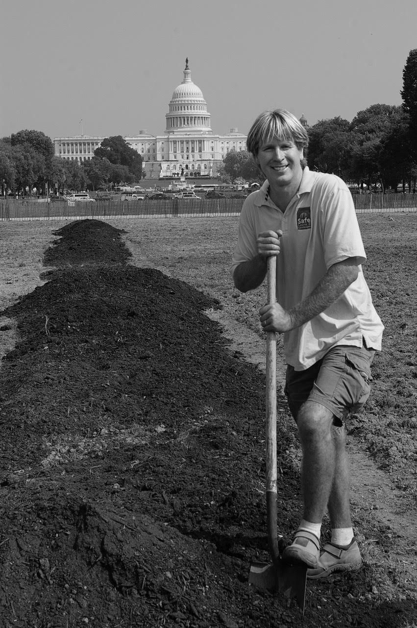 Paul Tukey leaning on a shovel beside rows of soil on the National Mall, with the U.S. Capitol behind him